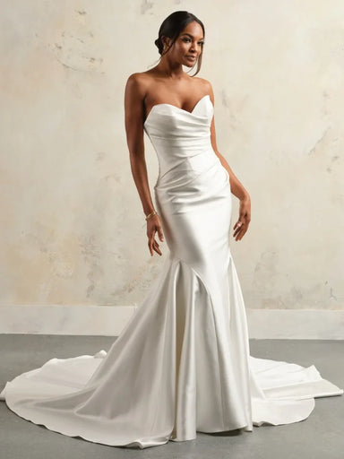 Woman wearing a white strapless wedding dress with a long train against a neutral background